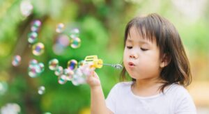 A young girl engaged in EYFS STEM activities at nursery, blowing bubbles outdoors, and exploring the properties of bubbles and surface tension.