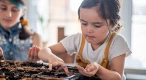 A young girl engaged in EYFS STEM activities, planting seeds in a pot with soil, and learning about plant life cycles and growth