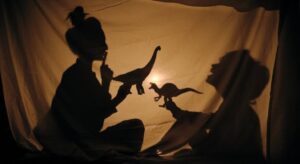 A young child engaged in STEM activities, playing with shadows and light with a nursery practitioner, exploring how different objects create shadows on a sheet.