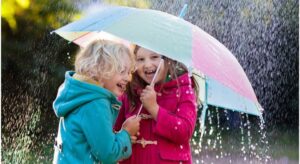 Two young children participating in STEM activities, playing in the rain under an umbrella, exploring weather patterns and discussing different types of weather.