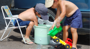 Two boys playing with toy cars in a bucket of water as part of a Water play activity called 'Car Wash Station.