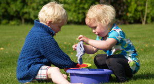 Two boys playing with buckets of water as part of water play at nursery.